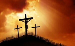 Silhouette of three crosses on a hill against a glowing golden sky with dramatic clouds and rays of light breaking through, symbolizing faith, sacrifice, and hope.
