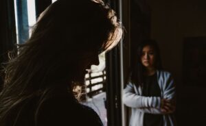 A shadowed woman looks down in regret while another watches, illustrating the struggle between false and true repentance.