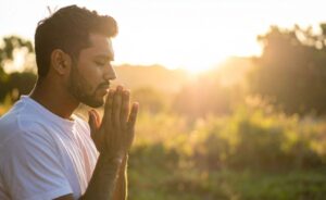 A man prays silently with eyes closed and hands pressed together outdoors, illustrating that God hears the heart's internal whispers without spoken words.