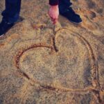 A person draws a large heart in the sand, representing the simple, quiet journey of letting God's Word define true love during this February reading plan.