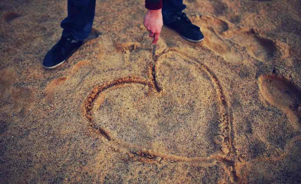 A person draws a large heart in the sand, representing the simple, quiet journey of letting God's Word define true love during this February reading plan.